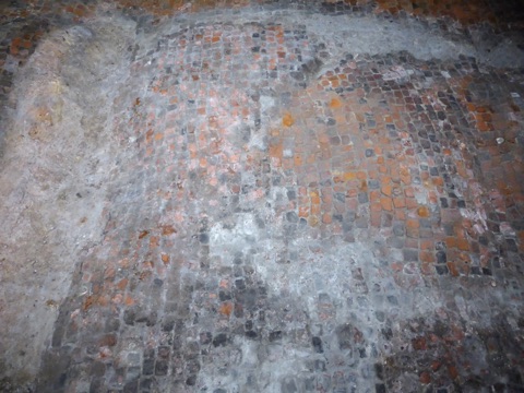 A patch of Roman floor of small square red and grey tiles, worn and uneven, set in grey mortar