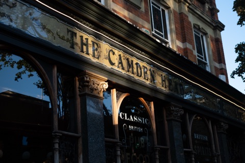 The Camden Head's Victorian pub front in low evening sun: gilt lettering on a dark fascia, etched glass, polished granite pilasters and red brick above.