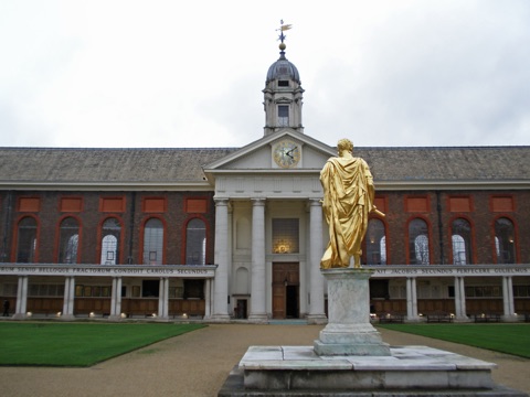 The Royal Hospital's Figure Court: a gilded statue of Charles II in Roman dress on a stone plinth, facing Wren's red-brick range with its white portico, clock and lantern, under a grey sky.