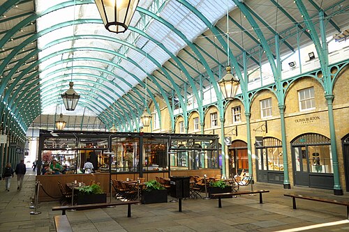 Inside Covent Garden Market: the glass-roofed arcade with lamps, café tables and shoppers along the central aisle