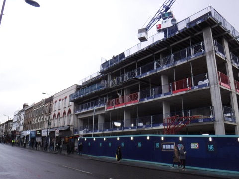 Kingsland High Street: a wide straight road lined with low shopfronts and flats above, buses and traffic running through, the street reaching away to the horizon.
