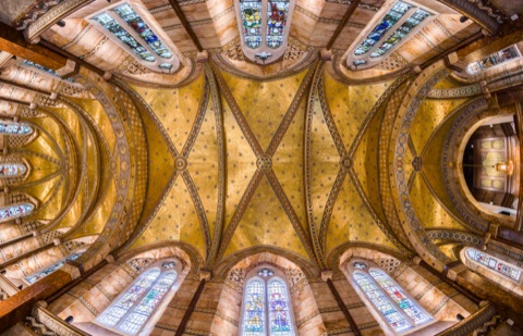 The ceiling of the Fitzrovia Chapel from below: gold mosaic vaults crossed by patterned ribs, marble-lined walls and stained-glass windows all round.