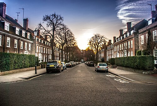 A quiet Kensington street of tall red-brick houses with white window frames and trees along the kerb