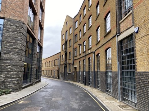 A curving street of yellow brick warehouses with iron-framed windows, converted to flats