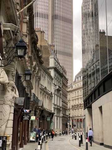 A narrow City lane between stone facades, with glass towers rising directly behind them