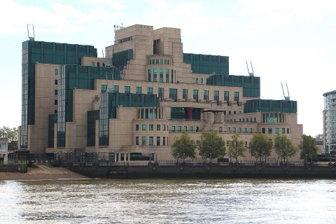 A stepped cream and green building on the far bank of the Thames, its terraces rising in blocks above the embankment wall, a line of trees along its front.