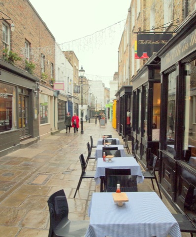 Camden Passage on a winter afternoon: café tables with gingham cloths out on the flagstones, shopfronts and fairy lights down the lane