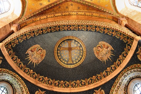 A domed mosaic ceiling of dark blue and gold: a cross in a starred roundel in the middle, an angel on either side holding a scroll, and bands of gold leaf pattern around the rim.