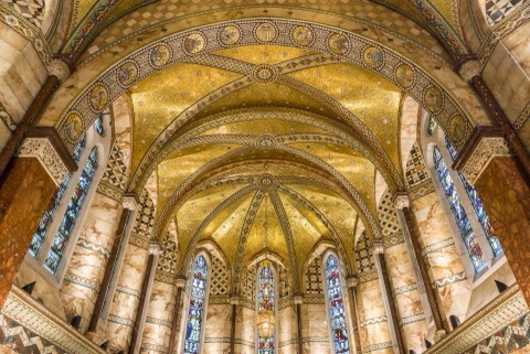 Looking east down the chapel: gold mosaic vaults studded with stars over marble-clad walls, a band of mosaic roundels along the arch, and tall stained-glass windows in the apse and on either side.
