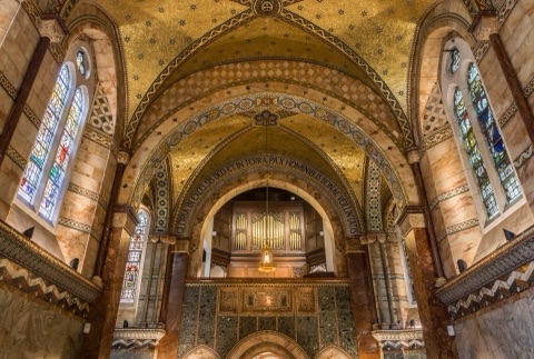 Looking west across the chapel to the organ gallery under its inscribed arch, the gold-starred vault above, stained-glass windows on either side and marble and mosaic walls below.