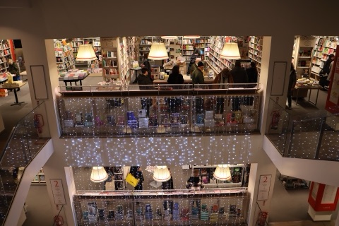 Looking down through the shop's central well: floors of white shelving full of books, big drum lampshades over the counters, and curtains of fairy lights hung across the void.