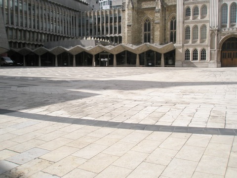 Guildhall Yard, paved in pale stone with a curved band of dark slabs across it tracing the amphitheatre's edge, with the Guildhall's stone front and the glazed gallery wing behind