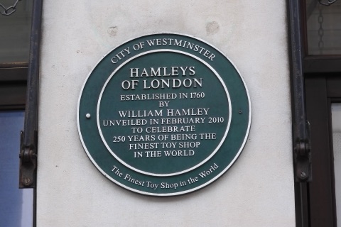 A round green City of Westminster plaque on a stone wall, reading Hamleys of London, established in 1760 by William Hamley, unveiled in February 2010 to celebrate 250 years of being the finest toy shop in the world.