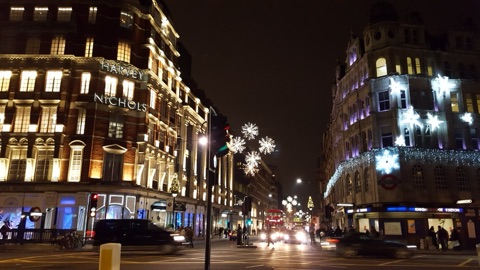 Knightsbridge at night in December: Harvey Nichols' name lit in white on its corner, snowflake lights strung over the road, a red bus among the traffic and the Underground station's lit front on the right.