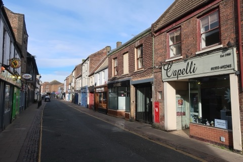 A narrow street of old brick shops and houses in low winter sun, a hairdresser's fascia on the right and a pub sign on the left, nobody about.