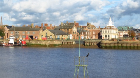 King's Lynn's quayside across the river: old brick warehouses, a pilot boat at the wall, and the white Custom House with its lantern tower, under a big sky.