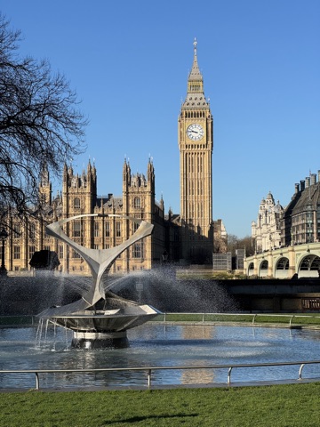 The Houses of Parliament and the Elizabeth Tower across the Thames on a clear winter day, seen over a stainless steel fountain playing in a round pool, with Westminster Bridge to the right.