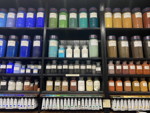 Rows of glass jars of blue, green and earth pigments on black shelving