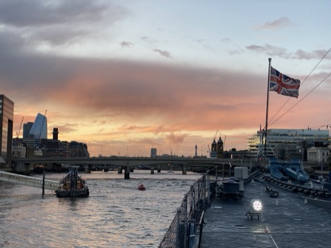 HMS Belfast's deck at sunset, the flag at the bow and the City upriver behind