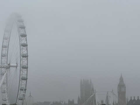 The London Eye in thick fog, the Houses of Parliament faint across the river