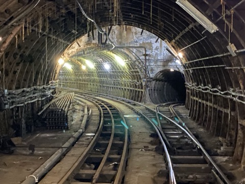 Tracks curving apart in a wide underground chamber, a second tunnel mouth opening to the right