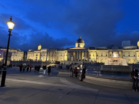 Trafalgar Square at dusk, the National Gallery lit behind the fountains
