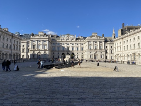 Somerset House's courtyard under a clear sky, the ranges around it and the fountain jets flat in the paving