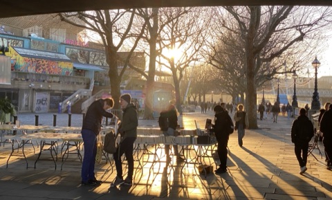 Book tables under Waterloo Bridge in low winter sun, browsers in silhouette