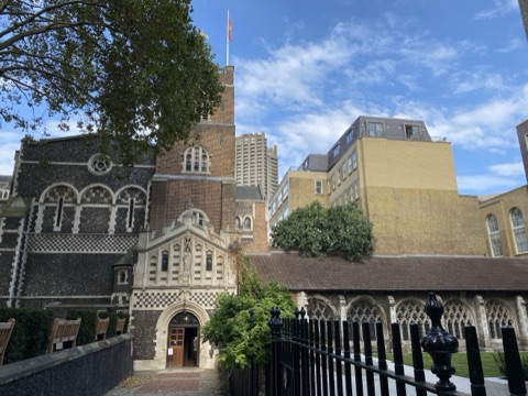 St Bartholomew the Great's chequered flint front and brick tower, modern City blocks rising behind