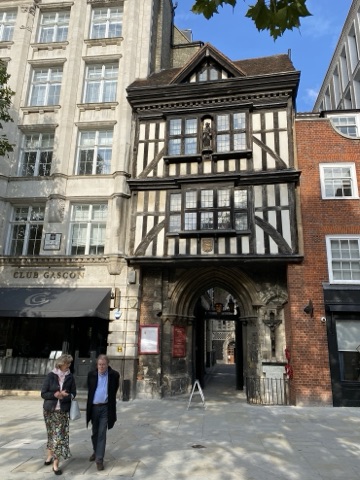 The timber-framed Tudor gatehouse above the stone arch into St Bartholomew the Great, two people walking past