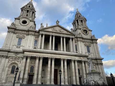 St Paul's west front in low sun: twin towers, a pediment and a columned porch, with the statue of Queen Anne in front