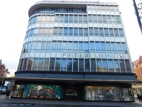 Peter Jones's curved glass front on Sloane Square: bands of windows in thin metal frames sweeping round the corner, the name in dark letters across the middle, and window displays at street level.