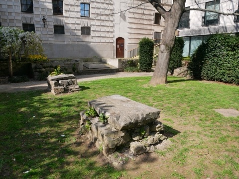 The stone footings of a demolished church standing in a City garden lawn, under a plane tree