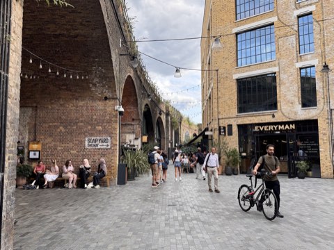 A paved lane under brick railway arches, festoon lights strung overhead and an Everyman cinema in the building opposite
