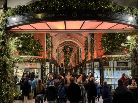 The Piccadilly entrance to Burlington Arcade at night, wreathed in Christmas greenery and lights, shoppers under the glass roof