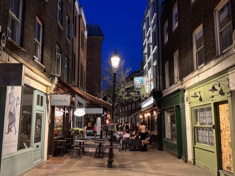 Charlotte Place at dusk, a lit lamppost in the middle of the lane and tables outside the restaurants