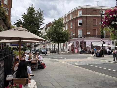 Pavement tables under a parasol on Ebury Street, with the pink-flowered corner shop on Elizabeth Street beyond