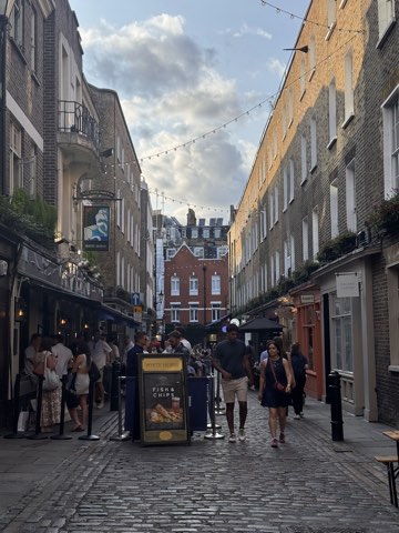 A cobbled pedestrian street behind Carnaby with festoon lights overhead, a pub on the left and a chip stand in the middle