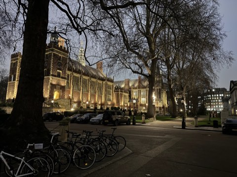The Great Hall and library of Lincoln's Inn lit at dusk, bicycles parked in the foreground and plane trees overhead