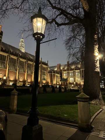 A lit lamppost in the foreground of Lincoln's Inn at night, the Great Hall floodlit behind the lawn