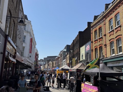 Lower Marsh on a bright weekday, market stalls down the middle and shopfronts either side