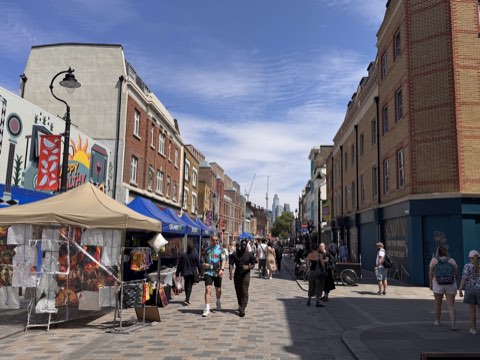 Lower Marsh on a sunny weekday, market stalls down one side and the City towers in the distance