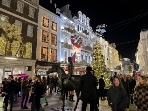 New Bond Street at night in December, shopfronts and trees strung with lights and a bronze equestrian statue in the middle of the pavement