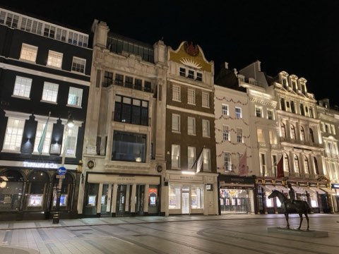 New Bond Street at night, lit shopfronts either side and an equestrian bronze on the pavement