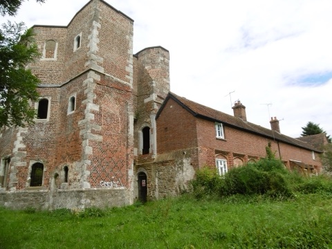 The surviving brick tower and gatehouse range of Otford Palace, its diapered Tudor brickwork with stone corners, and a row of cottages built into the old range, in long grass.