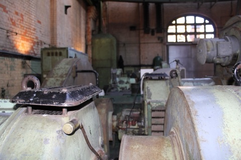 Inside the engine house: rows of pale green pumping machinery with rusting casings and brass fittings, brick walls and an arched window at the far end.