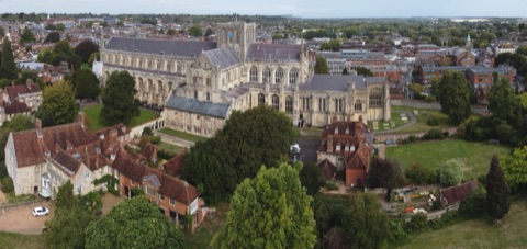 Winchester Cathedral from above: the long grey roof and squat central tower of the cathedral, with the Close's old houses and gardens in front and the town beyond.