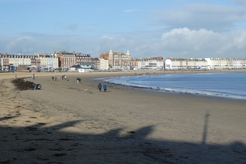 Weymouth's sandy beach curving round the bay to a seafront of Georgian terraces and hotels, a few people walking dogs on the sand in winter sun.